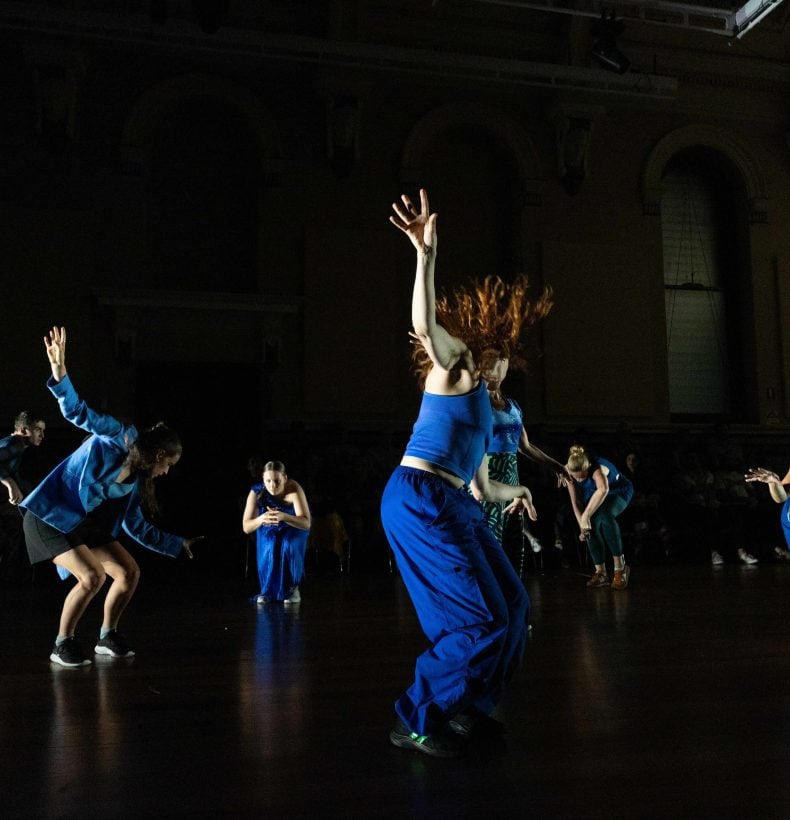 People dancing in a black room, wearing blue outfits.