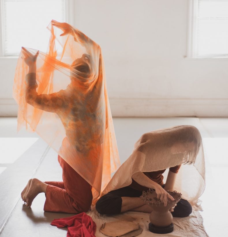 Two people performan under sheer fabric in an exhibition space.