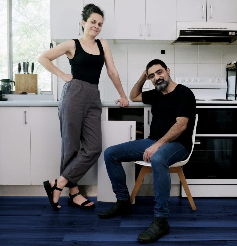 Two people casually pose for the camera in a kitchen.