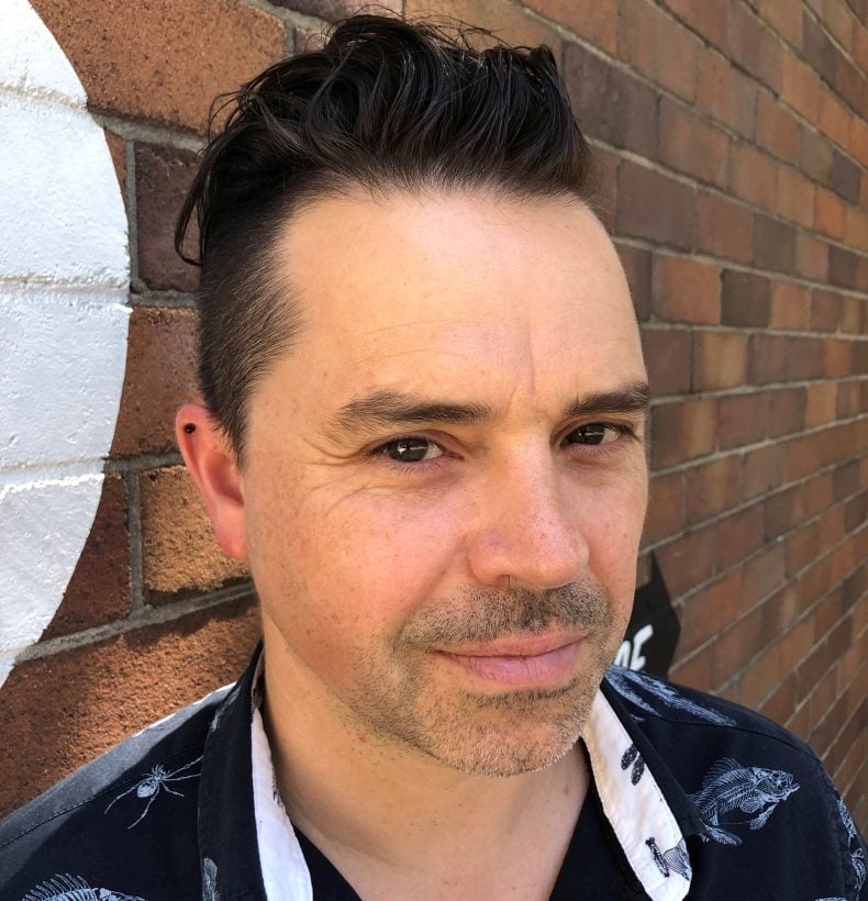 Man takes a selfie with a brick building background.