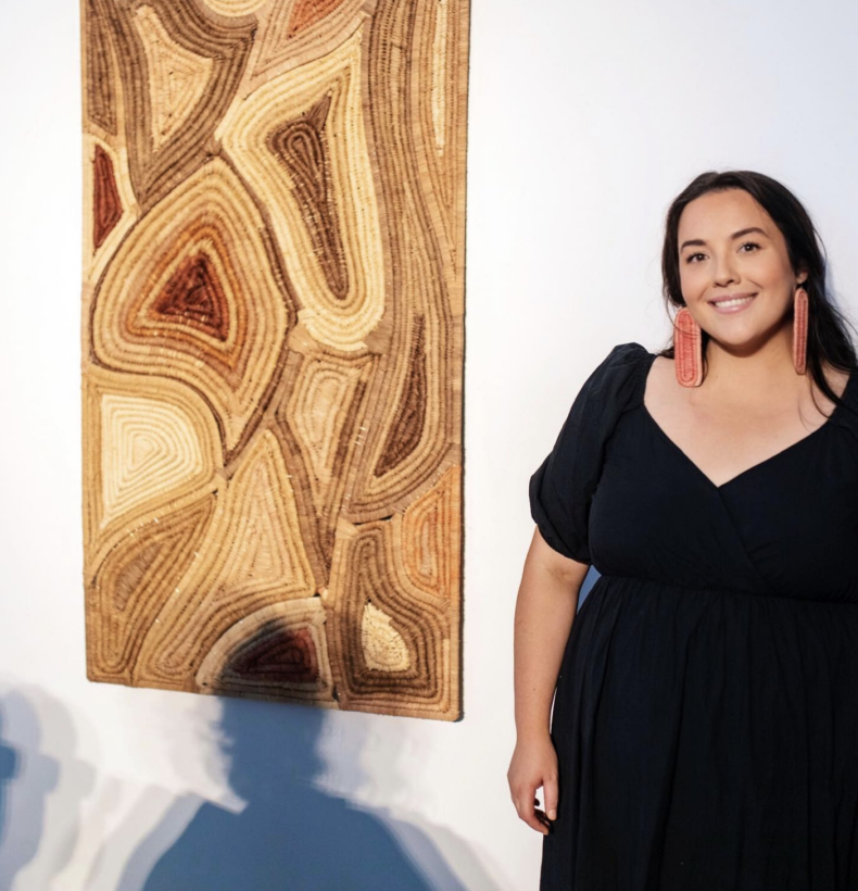 Woman poses next to artwork on the wall.