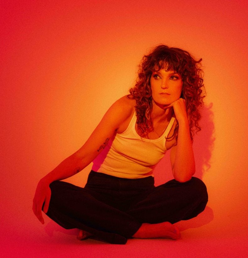 Woman sitting cross-legged in a studio that's lit up in orange lighting.