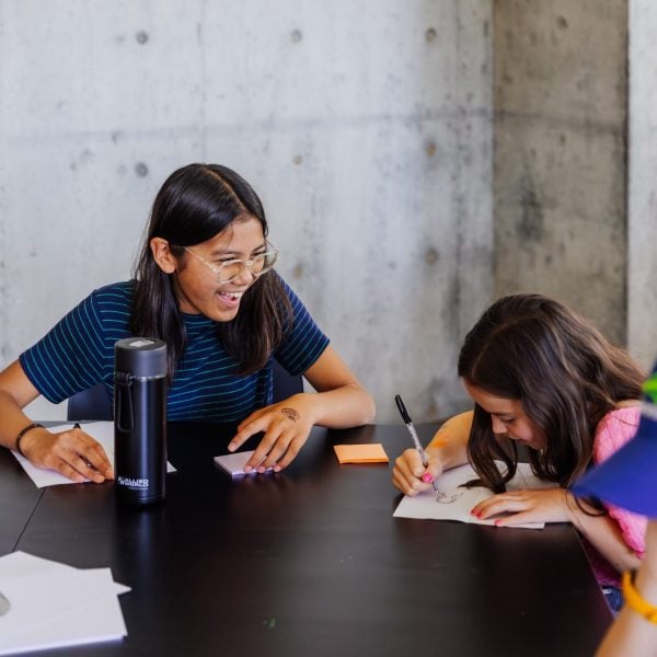 Kids laughing with writing pads on table.