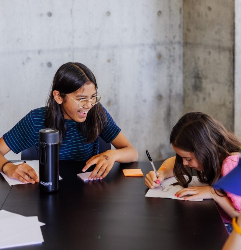 Kids laughing with writing pads on table.