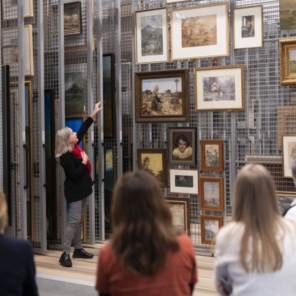 Woman showing other people a wall of paintings